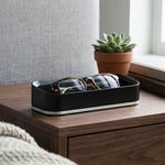 Black valet with glasses on a wooden nightstand next to a potted plant and books.