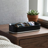 Black valet with glasses on a wooden nightstand next to a potted plant and books.