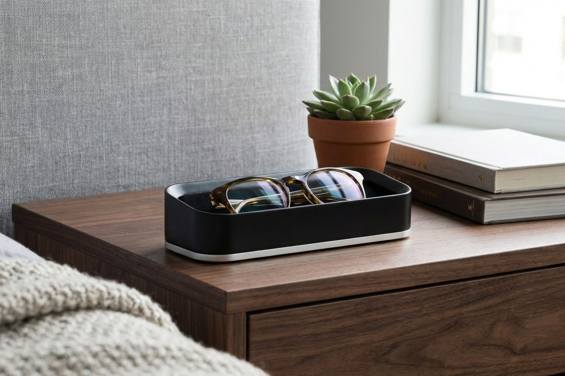 Black valet with glasses on a wooden nightstand next to a potted plant and books.