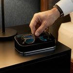 Person placing glasses into a black glasses valet on a nightstand.