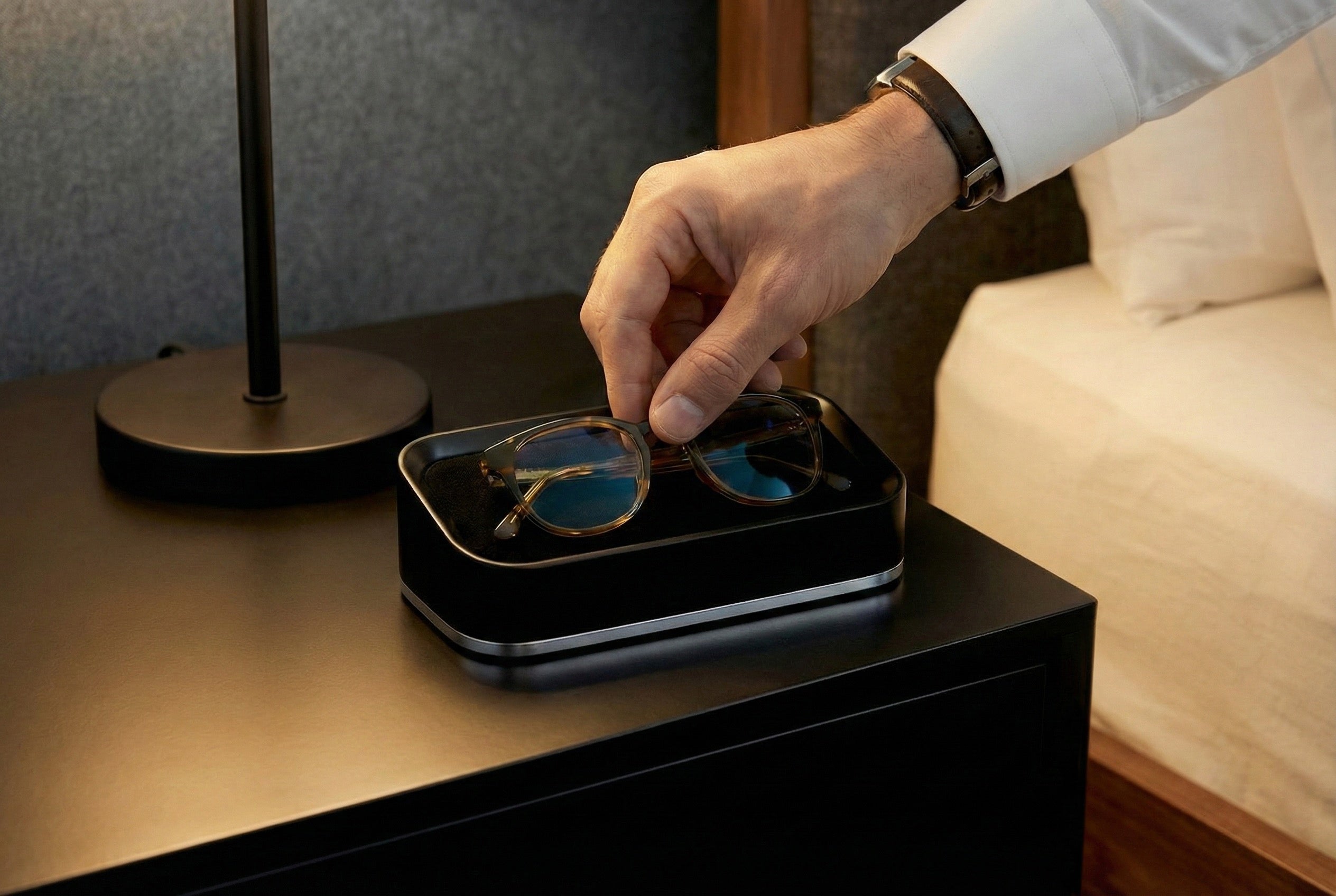 Person placing glasses into a black glasses valet on a nightstand.