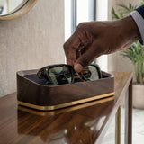 Man placing sunglasses into a walnut glasses valet in a luxurious home.
