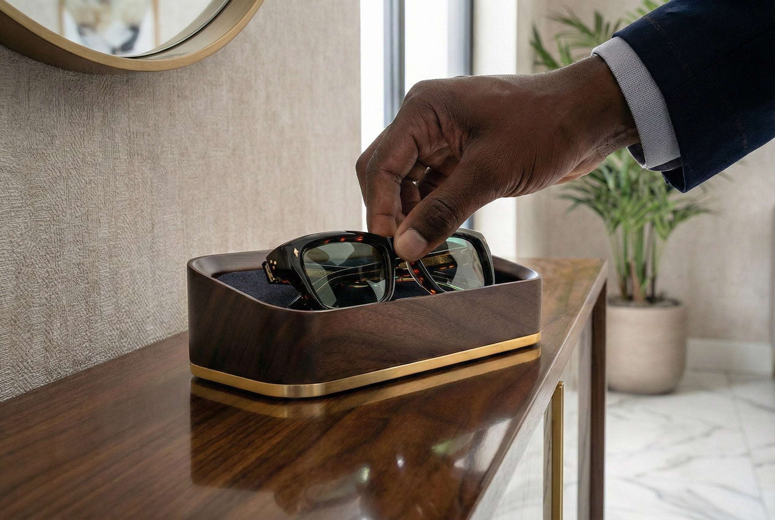 Man placing sunglasses into a walnut glasses valet in a luxurious home.